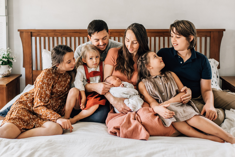 portrait of large family, parents with 5 children all sit on bed happy, newborn in moms arms