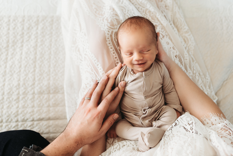Newborn Photography, parents hands hold happy baby laying in bed
